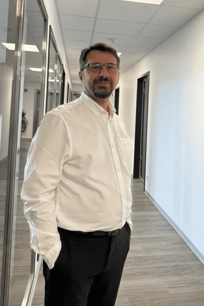 Steuerfachangestellter im weißen Hemd steht im Büroflur und blickt freundlich in die Kamera.